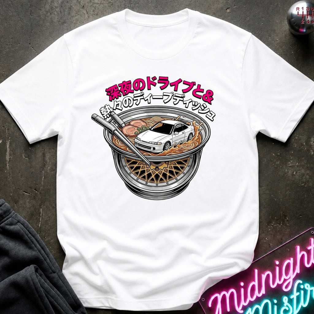 A white short-sleeve graphic T-shirt laid flat on a dark textured surface. The shirt features a large front print of a white sports car driving inside a ramen bowl, with pink and black Japanese text above.