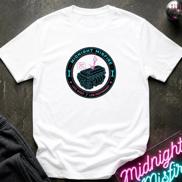 A white short-sleeve graphic t-shirt laid flat on a dark textured surface. The graphic features the text 'MIDNIGHT MISFIRE' above a silver sports car with smoke effects.