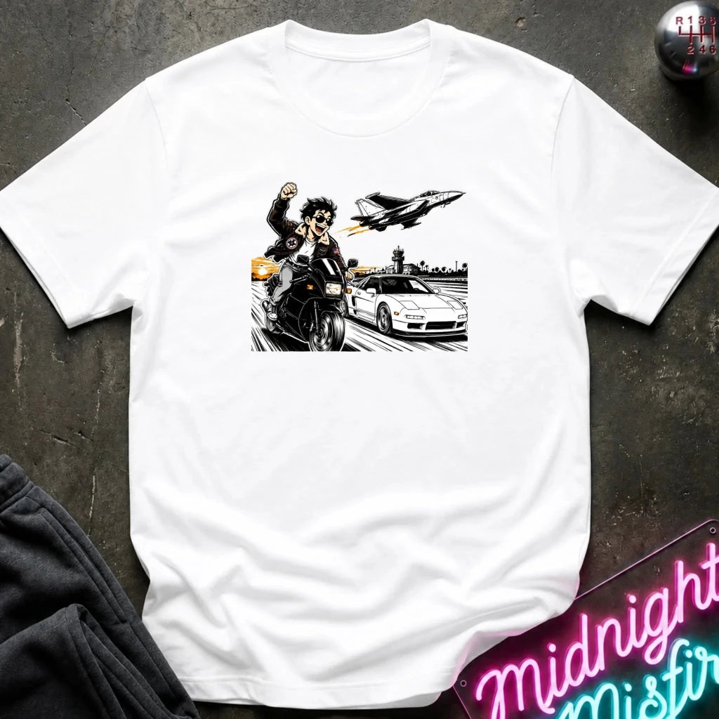A white short-sleeve crewneck t-shirt laid flat on a dark textured surface, featuring a black and white graphic print of a motorcycle racer, a sports car, and a jet plane.