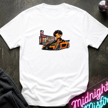 A white short-sleeve crewneck t-shirt laid flat on a dark textured surface, featuring a cartoon graphic of a man sitting on a orange and black sports car next to a store.