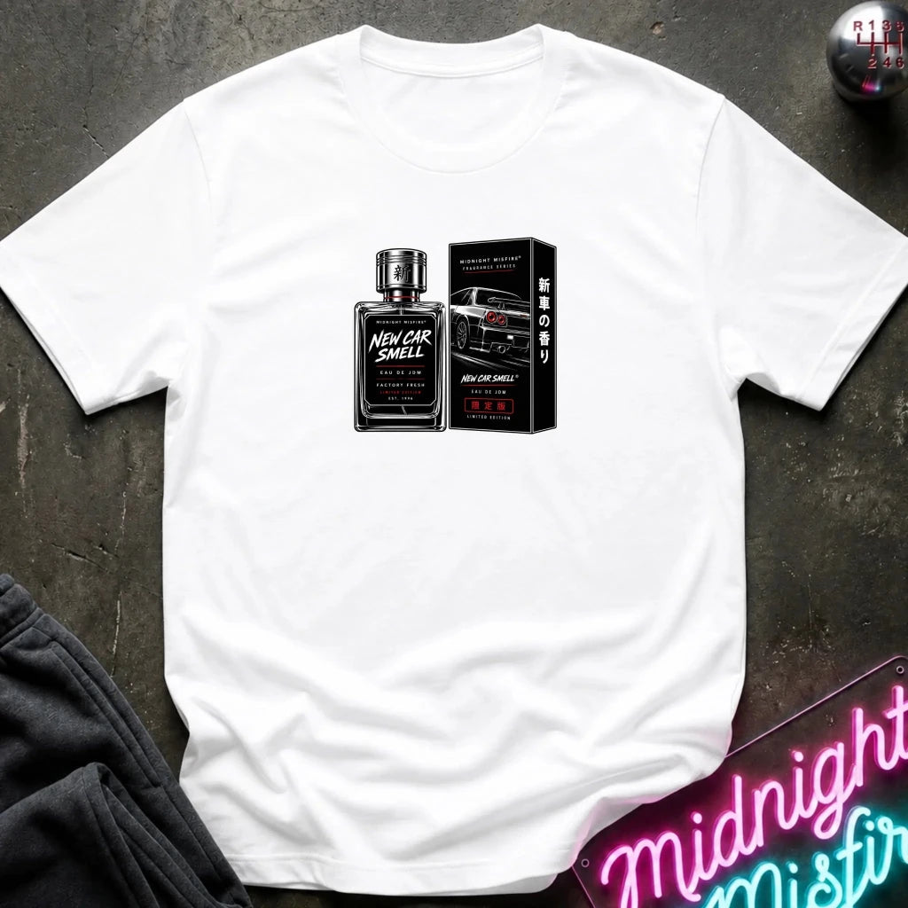 A white short-sleeve t-shirt laid flat on a dark textured surface, featuring a graphic print of a black perfume bottle and its box labeled 'New Car Smell'.