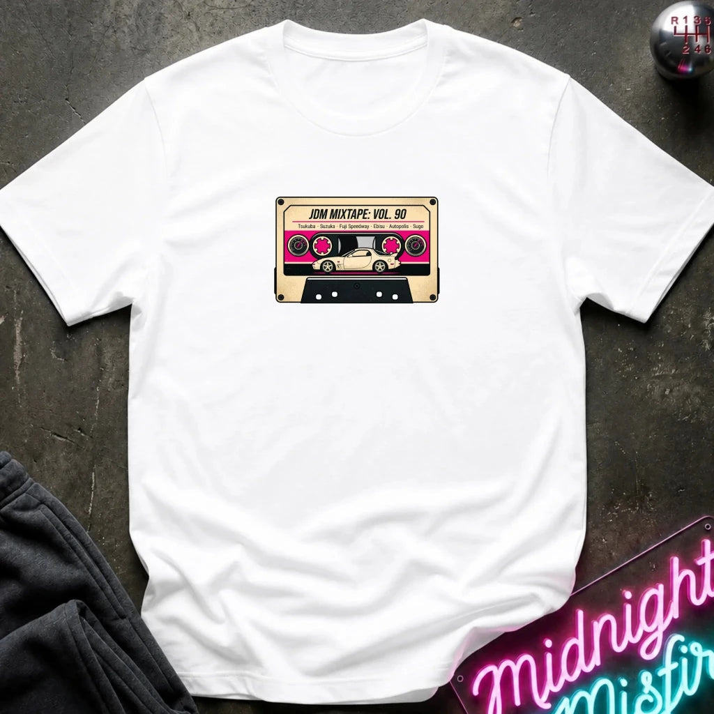 A white crewneck t-shirt laid flat on a dark textured surface, featuring a retro cassette tape graphic on the chest with the text 'JDM MIXTAPE VOL.