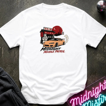 white crewneck t-shirt featuring a graphic print of a yellow Nissan Silvia S15 drift car in front of a red moon and Japanese storefront, with the text 'MIDNIGHT Noodle PATROL'. The shirt is laid flat on a dark textured surface with a neon sign and dark pants partially visible.