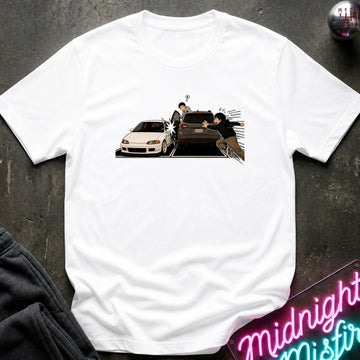 A white short-sleeve crewneck t-shirt laid flat on a dark textured surface, featuring a graphic print of a white sports car and a black SUV with character.