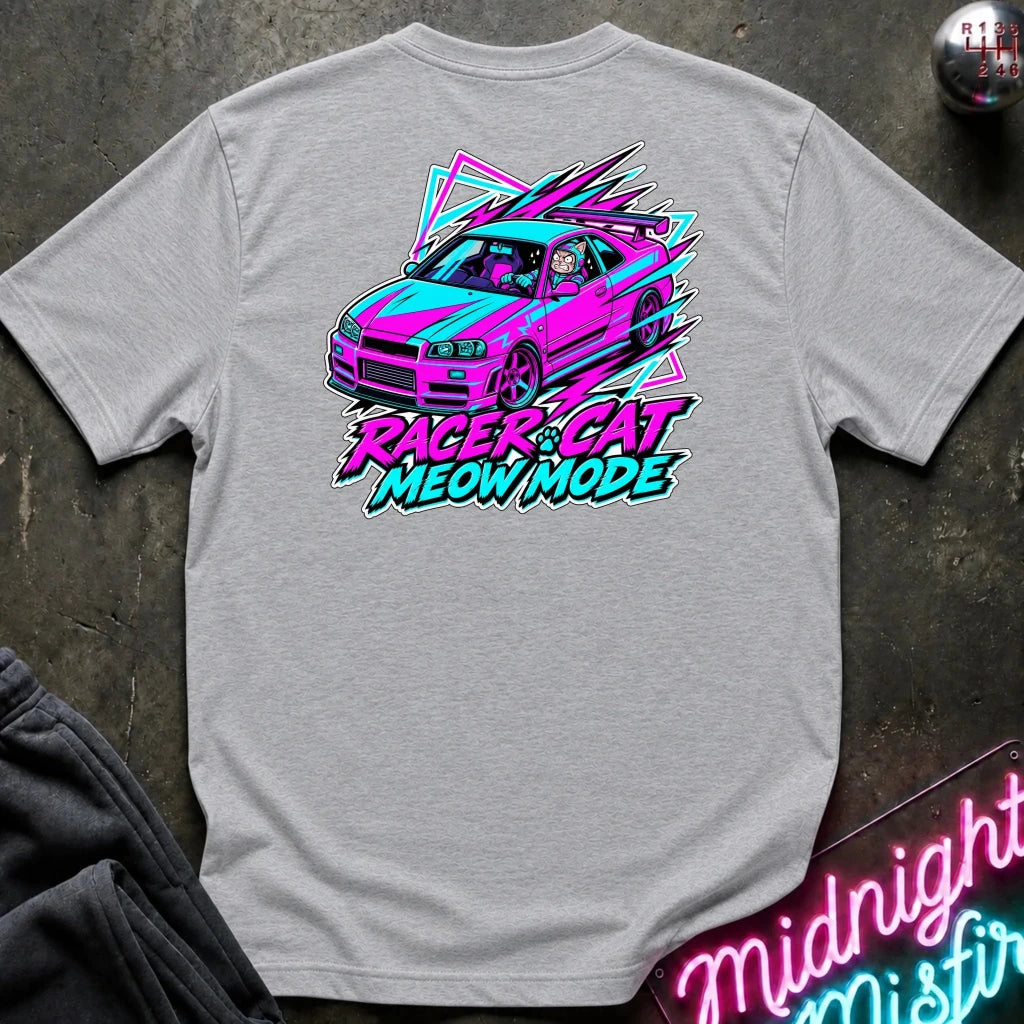 A light gray heather t-shirt laid flat on a dark textured surface, featuring a colorful graphic of a pink and blue race car with the text 'RACER CAT MEOW MODE' in neon pink and blue.