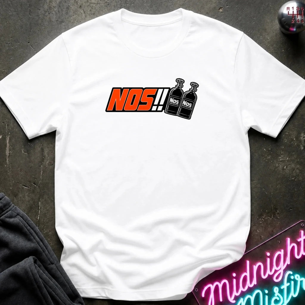 A white short-sleeve t-shirt laid flat on a dark textured surface, featuring a graphic print of the word 'NOS!!' in orange and black next to two black bottles labeled 'NOS'.