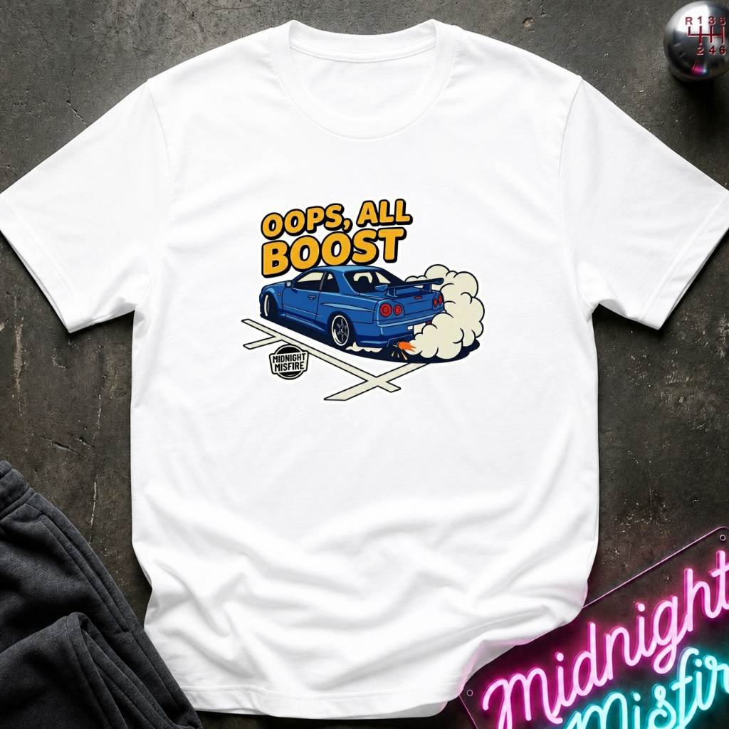 A white short-sleeve graphic t-shirt laid flat on a dark textured surface. The graphic features a blue sports car with smoke and the text 'OOPS, ALL BOOST' in yellow and orange.