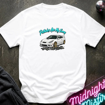A white short-sleeve t-shirt laid flat on a dark textured surface, featuring a graphic of a white sports car with gold wheels and the text 'Petrols Are My Enemy' in teal. A neon sign and dark clothing are partially visible in the corners.