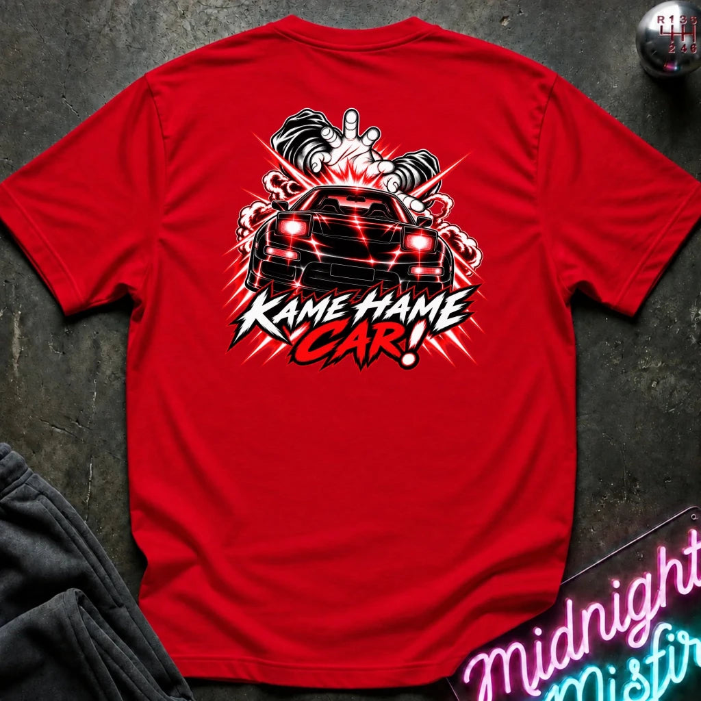 A red short-sleeve graphic T-shirt laid flat on a dark textured surface. The back of the shirt features a large black, white, and red graphic of a sports car with flames and the text 'KAME HAME CAR!'.