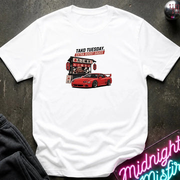 A white short-sleeve t-shirt laid flat on a dark textured surface, featuring a graphic print of a red sports car and a Japanese-style restaurant sign with the text 'TAKO TUESDAY' 