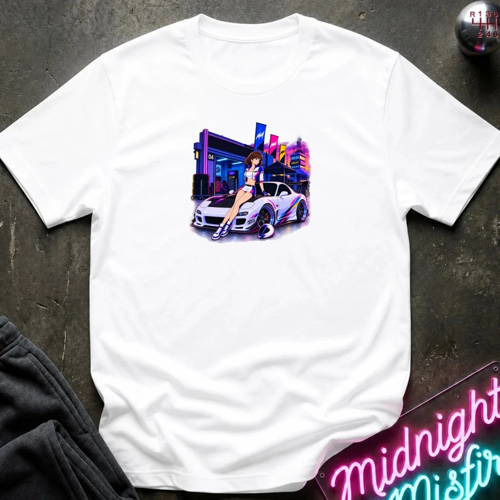 A white short-sleeve t-shirt laid flat on a dark textured surface, featuring a colorful graphic print of a white sports car and a woman in a neon-lit scene. 