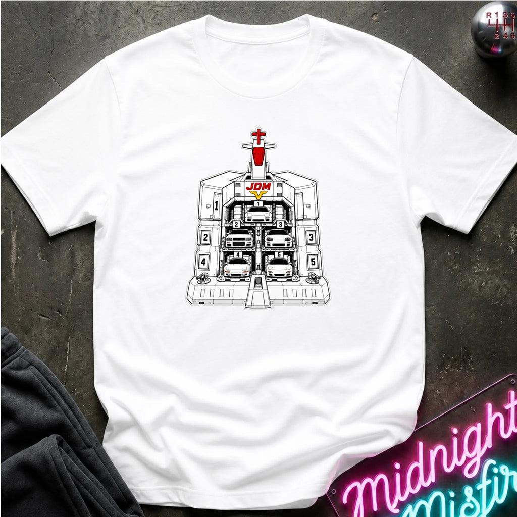 A white short-sleeve crewneck t-shirt laid flat on a dark textured surface, featuring a black and white graphic of the JDM (Japanese Domestic Market) cars in a launch bay.