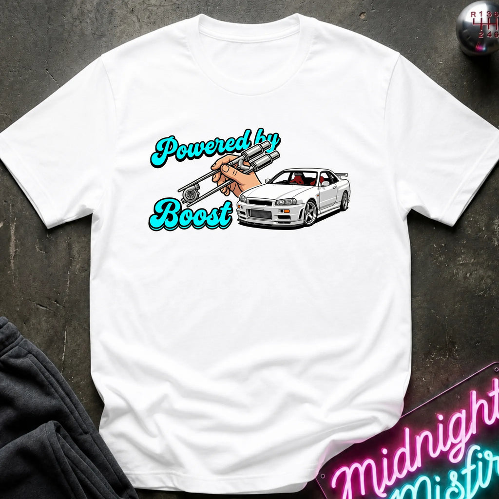 A white graphic t-shirt laid flat on a dark textured surface. The graphic features the text 'Powered by Boost' in a teal cursive font, with a hand holding a silver turbocharger, alongside a white sports car.