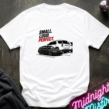 A white short-sleeve graphic T-shirt laid flat on a dark textured surface. The shirt features a printed design.