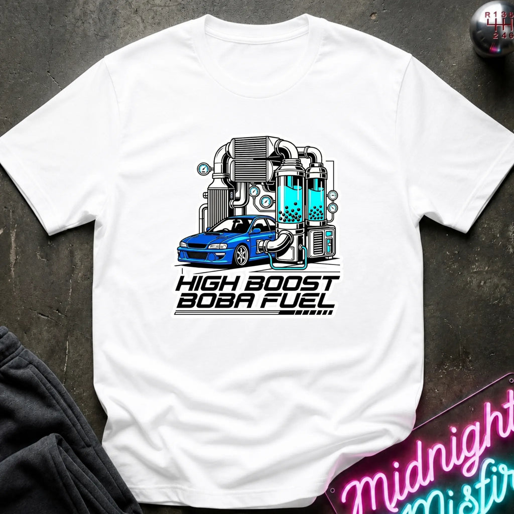 A white short-sleeve t-shirt laid flat on a dark textured surface, featuring a graphic of a blue car connected to a teal and gray high-performance turbo system with the text 'HIGH BOOST BOBA FUEL'.