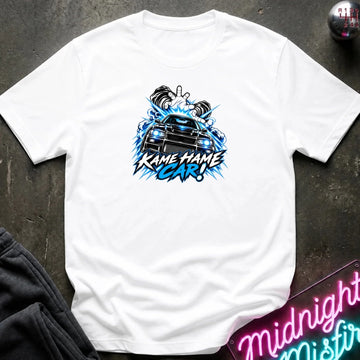 white short-sleeve graphic t-shirt laid flat on a dark textured surface. The shirt features a red, white, and black graphic of a car with the text 'KAME HAME CAR!' in stylized lettering.