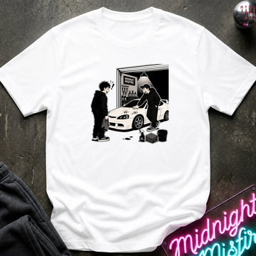 A white short-sleeve crewneck t-shirt laid flat on a dark textured surface, featuring a black and white graphic print of a character in a black hoodie standing next to a white sports car in front of a garage.