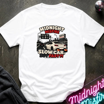 A white short-sleeve graphic t-shirt laid flat on a dark textured surface. The graphic features a white sports car on a highway with the text 'MIDNIGHT MISFIRE SLOW CAR BUT FAST!!' in stylized red, black, and white lettering.