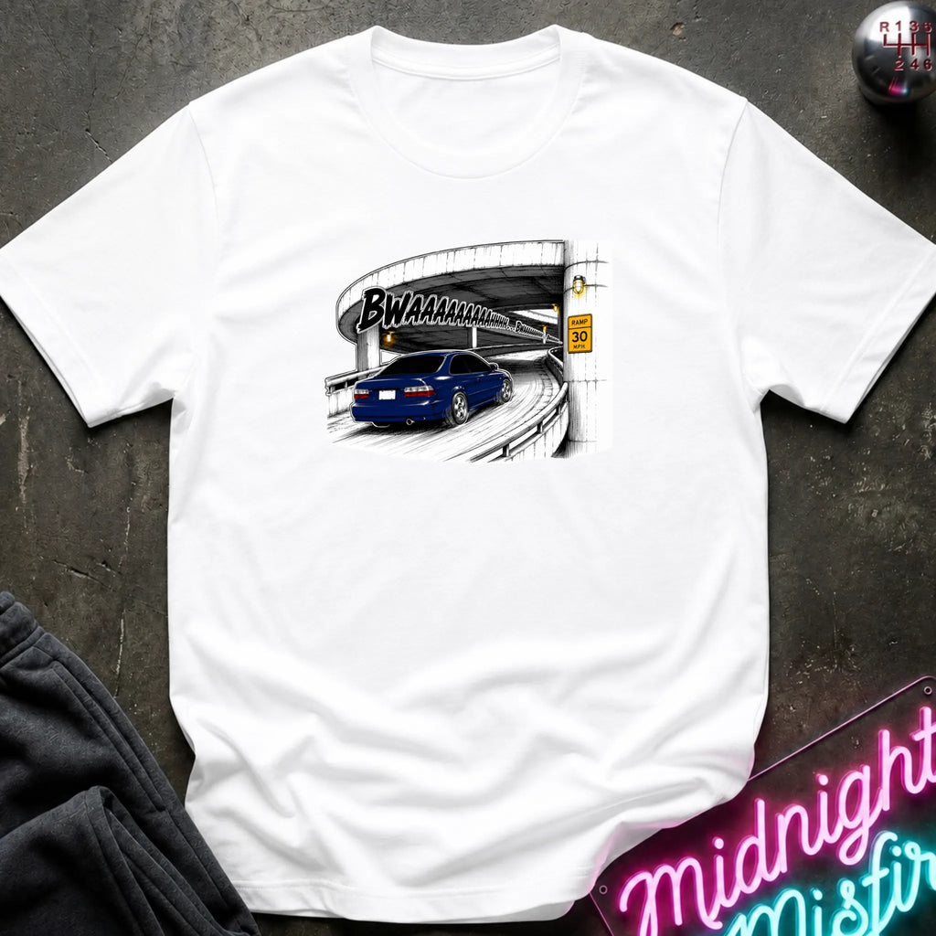 A white short-sleeve crewneck t-shirt laid flat on a dark textured surface. The shirt features a graphic print of a blue car driving under a highway overpass with the text 'BWAHAHA'.