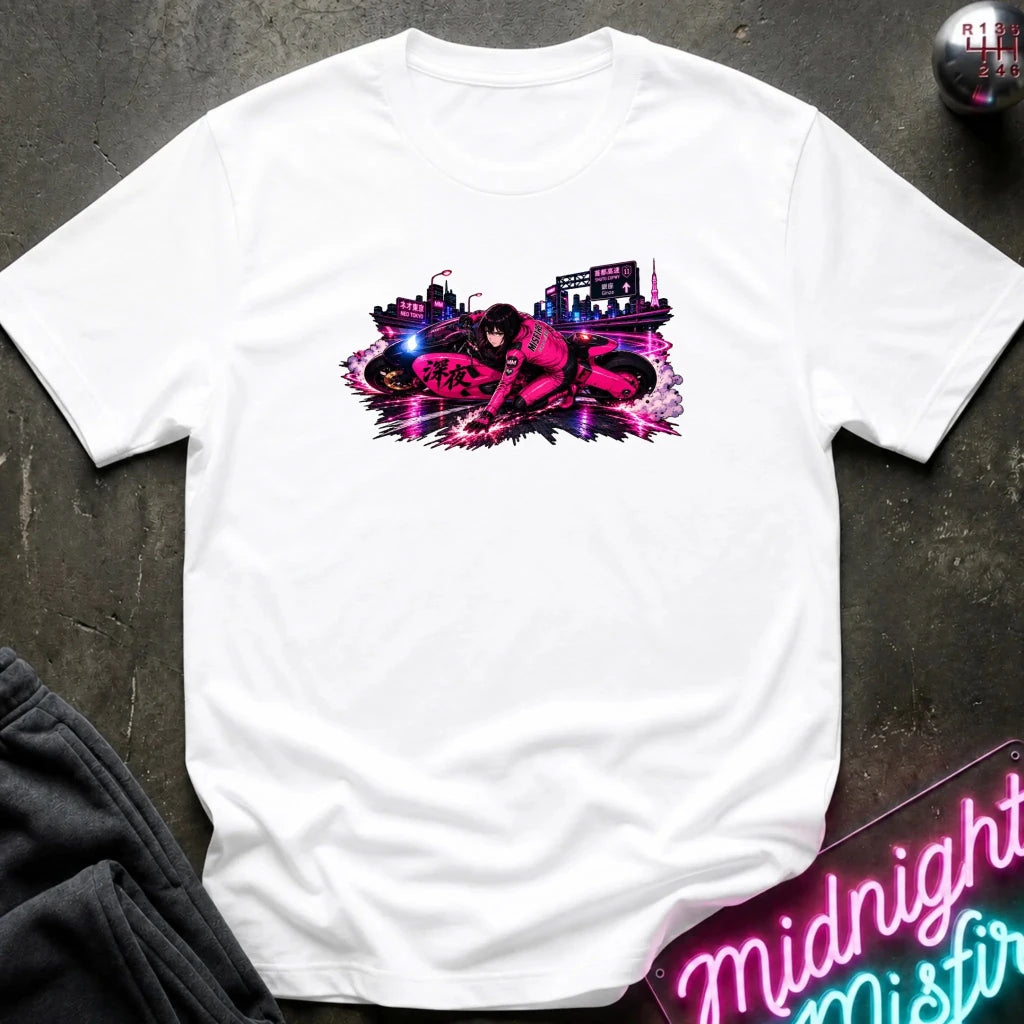 A white short-sleeve t-shirt laid flat on a dark textured surface, featuring a vibrant pink and purple graphic print of a motorcycle racer on the chest. The shirt is styled with dark gray sweatpants, a neon sign, and a small decorative object in the corners.