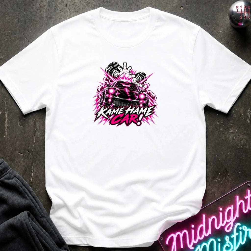 white short-sleeve graphic t-shirt laid flat on a dark textured surface. The shirt features a red, white, and black graphic of a car with the text 'KAME HAME CAR!' in stylized lettering.