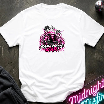 white short-sleeve graphic t-shirt laid flat on a dark textured surface. The shirt features a red, white, and black graphic of a car with the text 'KAME HAME CAR!' in stylized lettering.