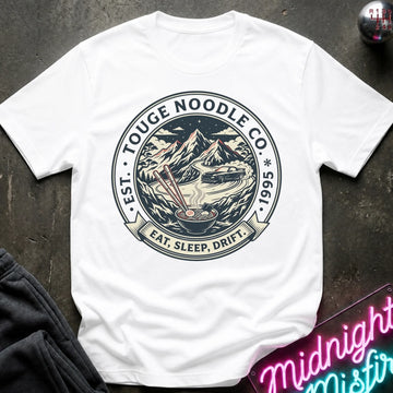 White short-sleeve graphic T-shirt laid flat on a dark textured surface. The shirt features a large circular vintage-style print in the center with mountains, chopsticks, a bowl, and the text 'EAT.