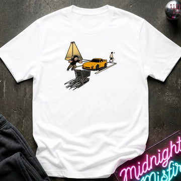 A white short-sleeve t-shirt laid flat on a dark textured surface, featuring a graphic print of a yellow sports car, a shopping cart, a lamp, and a small figure. 