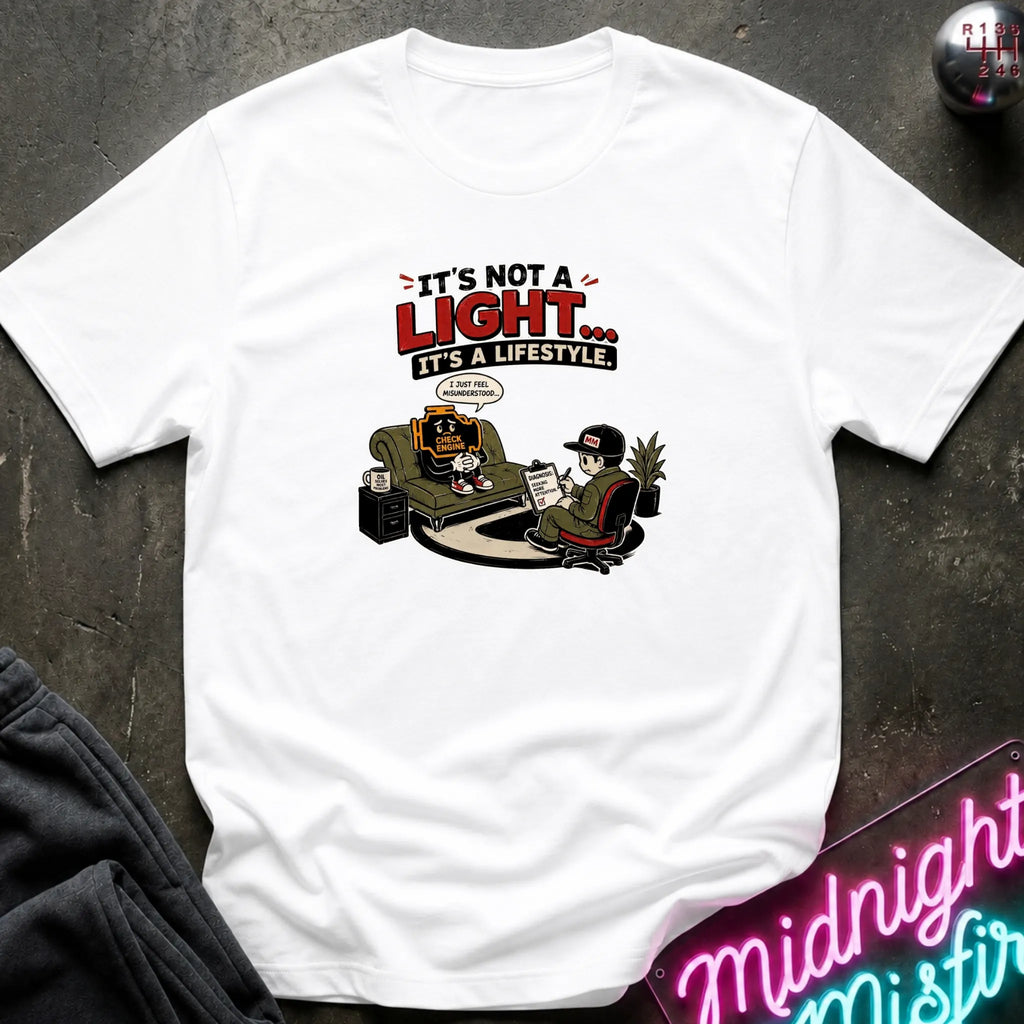 A white short-sleeve graphic t-shirt laid flat on a dark textured surface. The graphic features the text 'IT'S NOT A LIGHT.