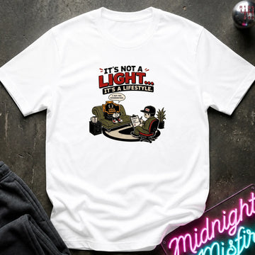 A white short-sleeve graphic t-shirt laid flat on a dark textured surface. The graphic features the text 'IT'S NOT A LIGHT.