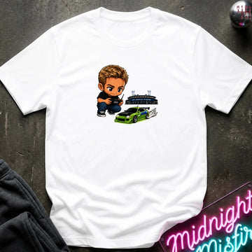 A white graphic t-shirt laid flat on a dark textured surface. The graphic features a green car, and person  controlling it with remote.