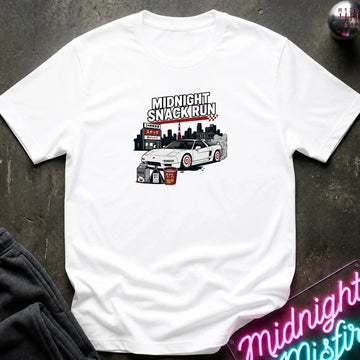 A white short-sleeve graphic t-shirt laid flat on a dark textured surface. The graphic features a white sports car with red wheels and black text reading 'MIDNIGHT SNACKIRUN' above it.
