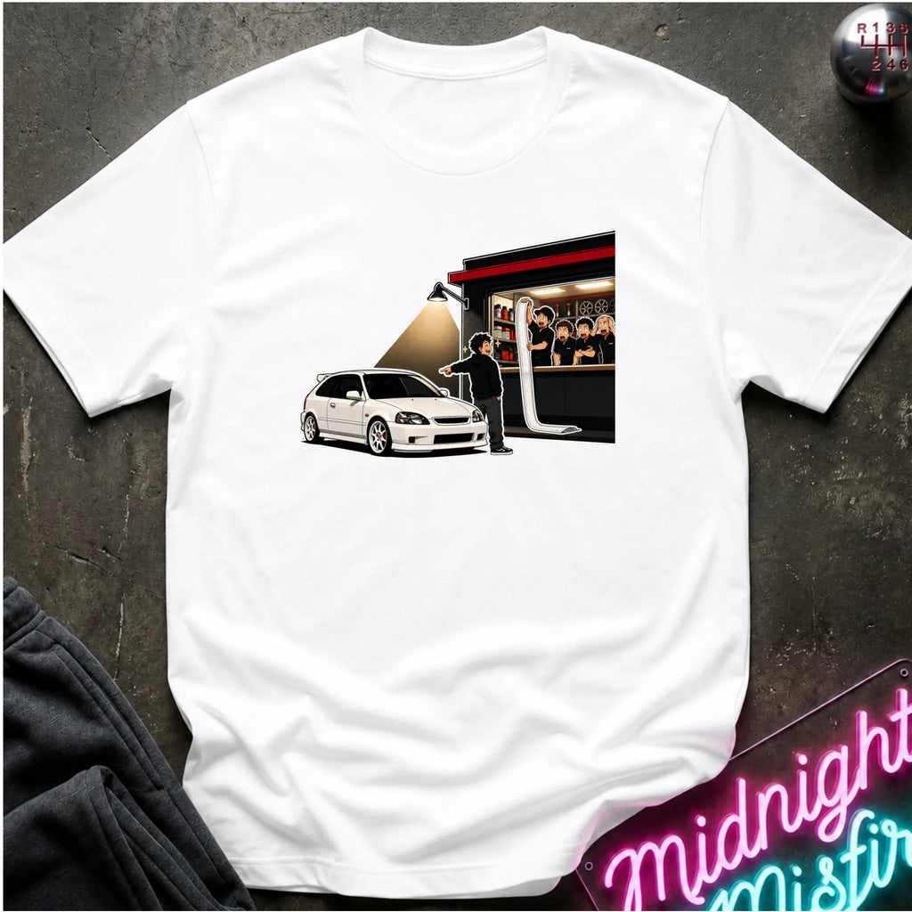 A white short-sleeve crewneck t-shirt laid flat on a dark textured surface. The front of the shirt features a rectangular graphic print depicting a white hatchback car, a person standing, and a building with people inside.