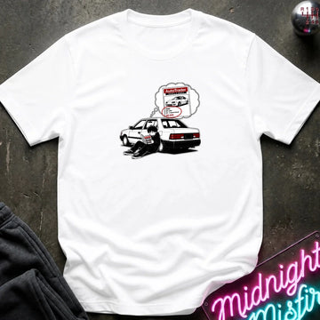 A white short-sleeve t-shirt laid flat on a dark textured surface, featuring a graphic of a black-and-whitecar with a thought bubble showing a car part diagram.