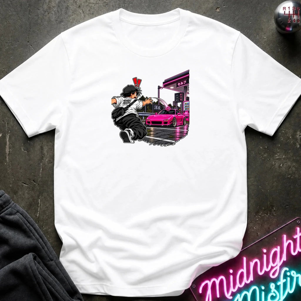 A white short-sleeve crewneck t-shirt laid flat on a dark textured surface. The center of the shirt features a graphic print of an anime character in a black and white outfit with a hat, next to a sports car 