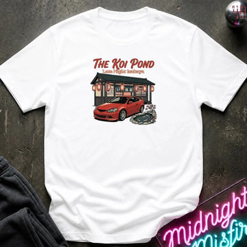 A white short-sleeve graphic t-shirt laid flat on a dark textured surface. The graphic features the text 'THE KOI POND Late Night Hamburger' above an illustration of a red sports car parked in front of a restaurant with red lanterns and a koi pond.