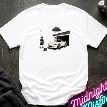 A white short-sleeve t-shirt laid flat on a dark textured surface, featuring a black and white graphic print of a person washing a white sports car outside a garage under a dark cloud.