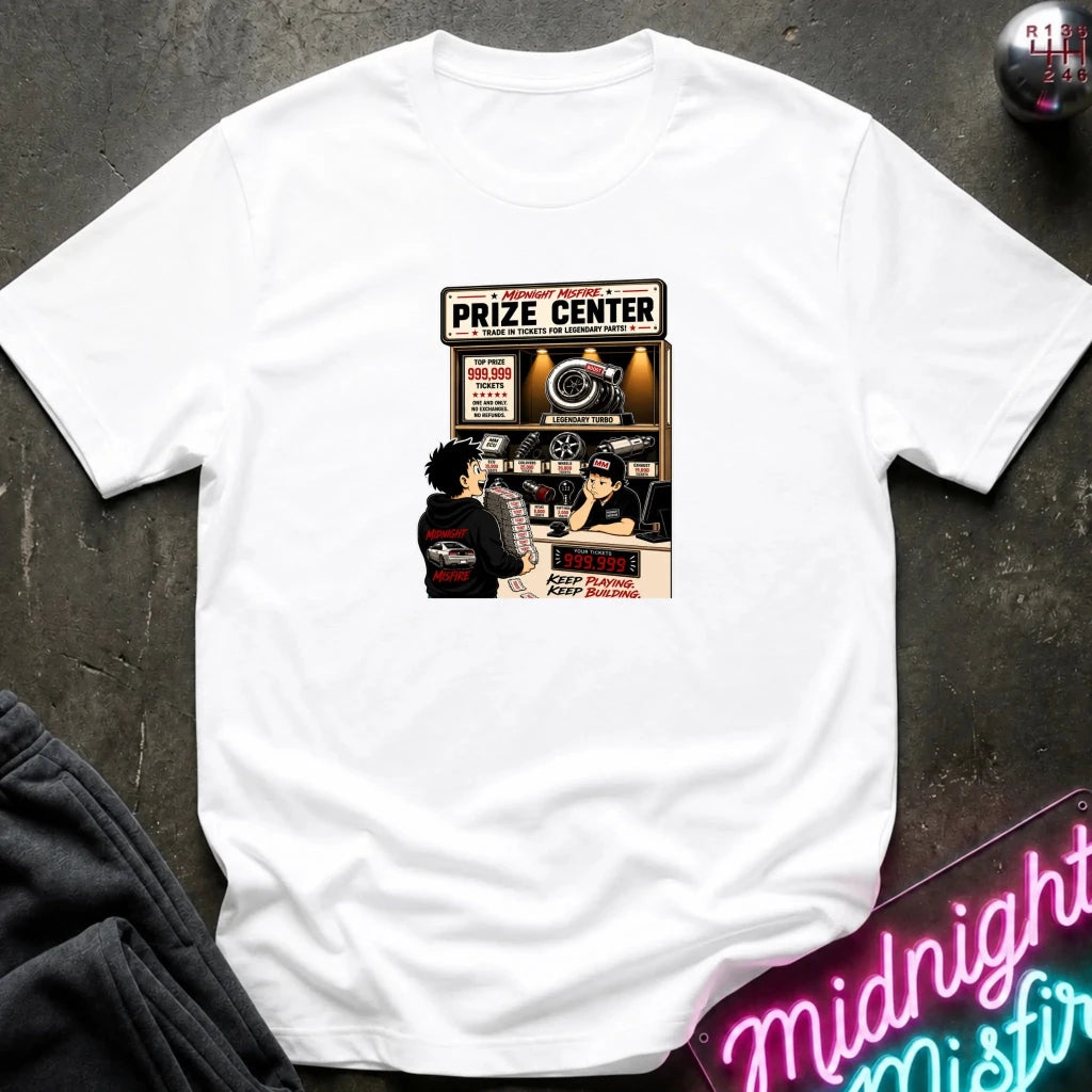 A white short-sleeve crewneck t-shirt laid flat on a dark textured surface, featuring a vintage-style graphic print of a 'Prize Center' with illustrated characters and neon signs in the background.