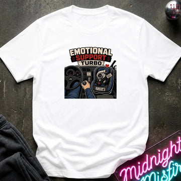 A white short-sleeve graphic T-shirt laid flat on a dark textured surface. The shirt features a central graphic with the text 'EMOTIONAL SUPPORT TURBO' above an illustration of a car interior with a hand on the steering wheel.