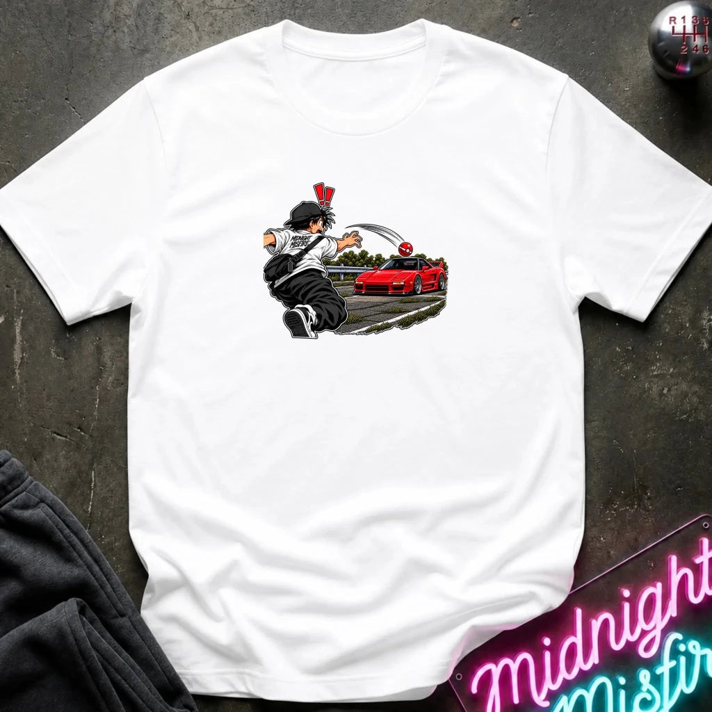 A white short-sleeve crewneck t-shirt laid flat on a dark textured surface. The center of the shirt features a graphic print of an anime character in a black and white outfit with a hat, next to a sports car 