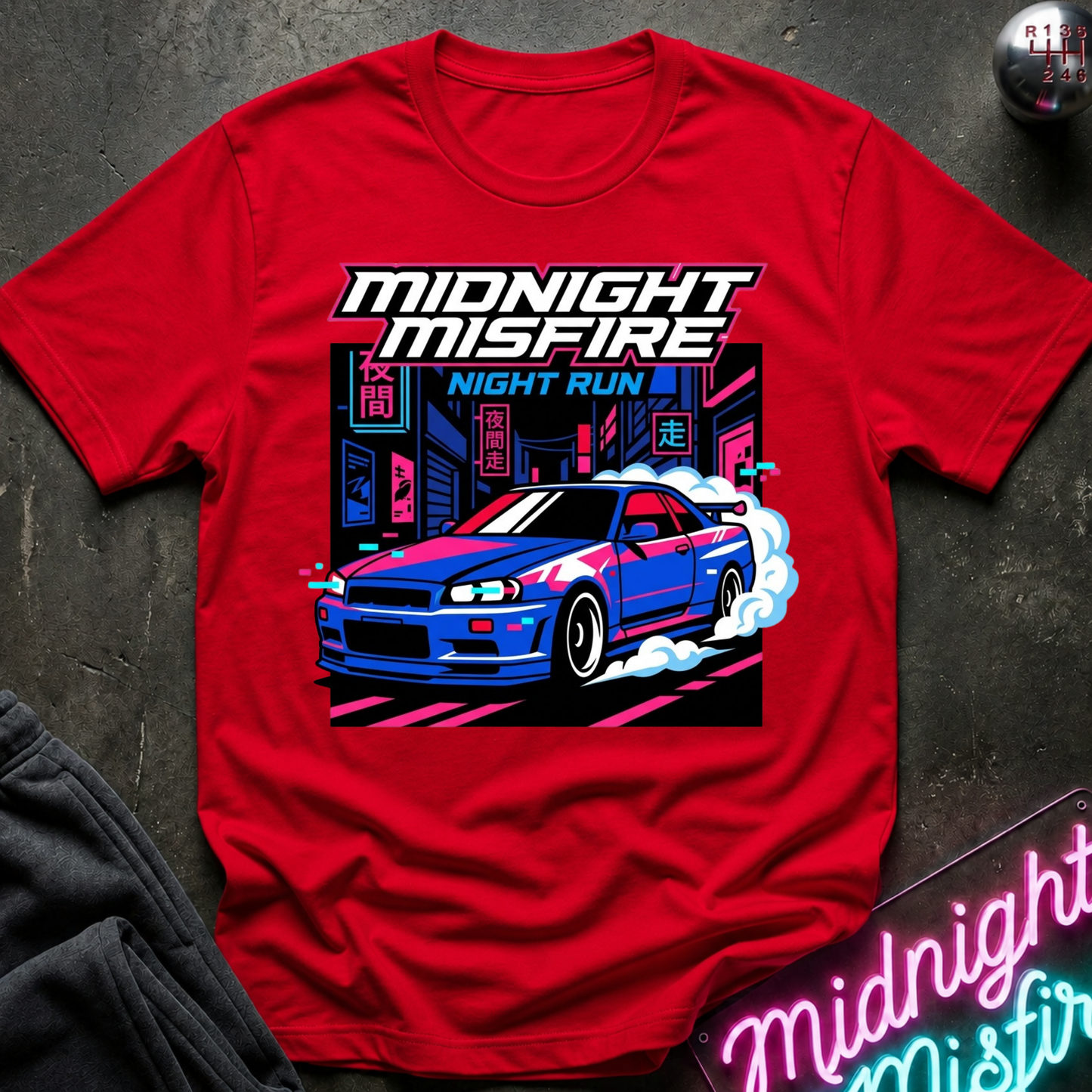 A red short-sleeve graphic T-shirt laid flat on a dark textured surface. The shirt features a large front print with the words “MIDNIGHT MISFIRE” and “NIGHT RUN,” plus a stylized blue and white sports car with pink neon city elements.