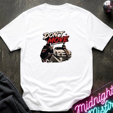 A white short-sleeve graphic t-shirt laid flat on a dark textured surface. The graphic features the words 'DON'T MOVE' in a stylized red and black font above an illustration of a person crouching next to a white sports car.