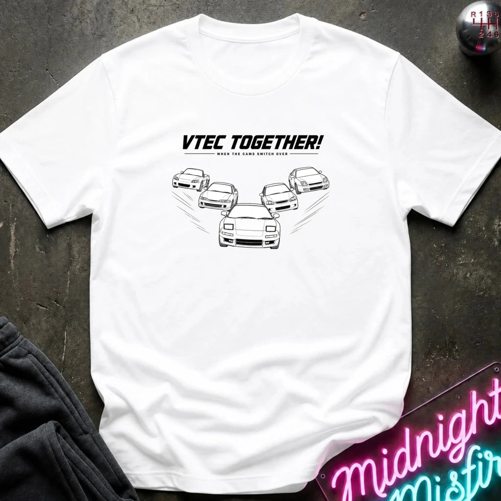 A white short-sleeve graphic T-shirt laid flat on a dark textured surface. The shirt features a black line-art graphic of several cars with the text 'VTEC TOGETHER!' 