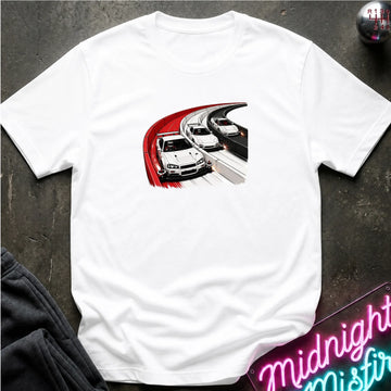 A white short-sleeve t-shirt laid flat on a dark textured surface, featuring a graphic print of three racing cars on a curved track with red and black motion lines. A neon sign and dark pants are partially visible as props.