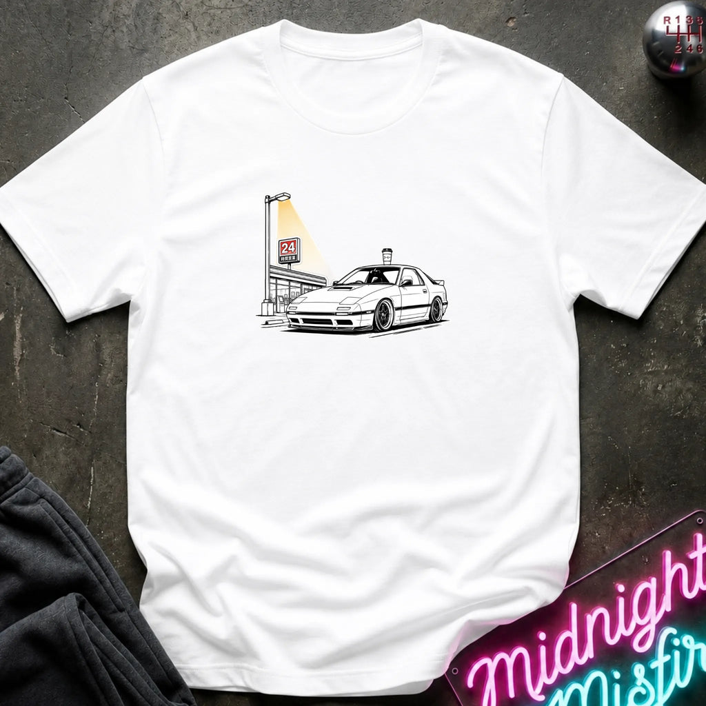 A white short-sleeve crewneck t-shirt laid flat on a dark textured surface, featuring a black line art graphic of a white sports car parked next to a lit street lamp.