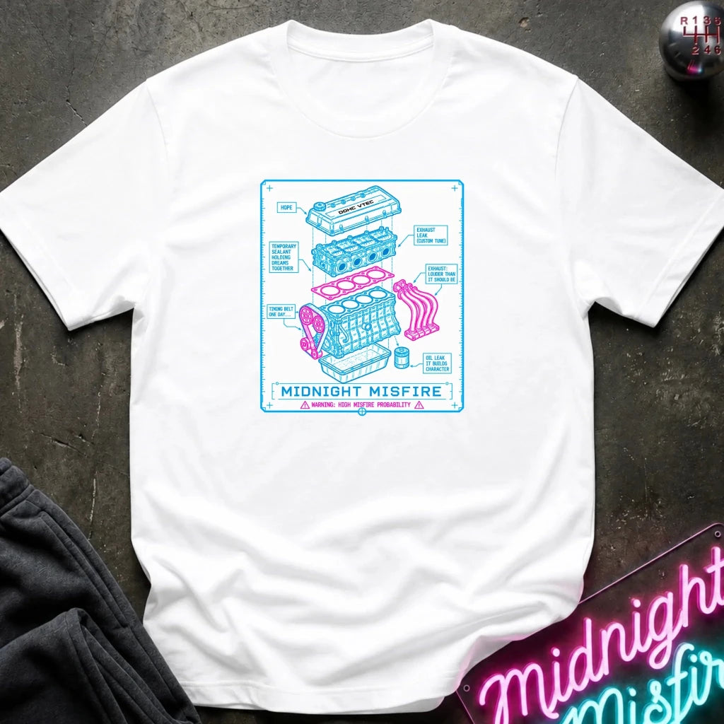 white short-sleeve graphic T-shirt laid flat on a dark textured surface. The shirt features a centered rectangular print with a light blue and pink exploded-style engine diagram and the text 'MIDNIGHT MISFIRE.