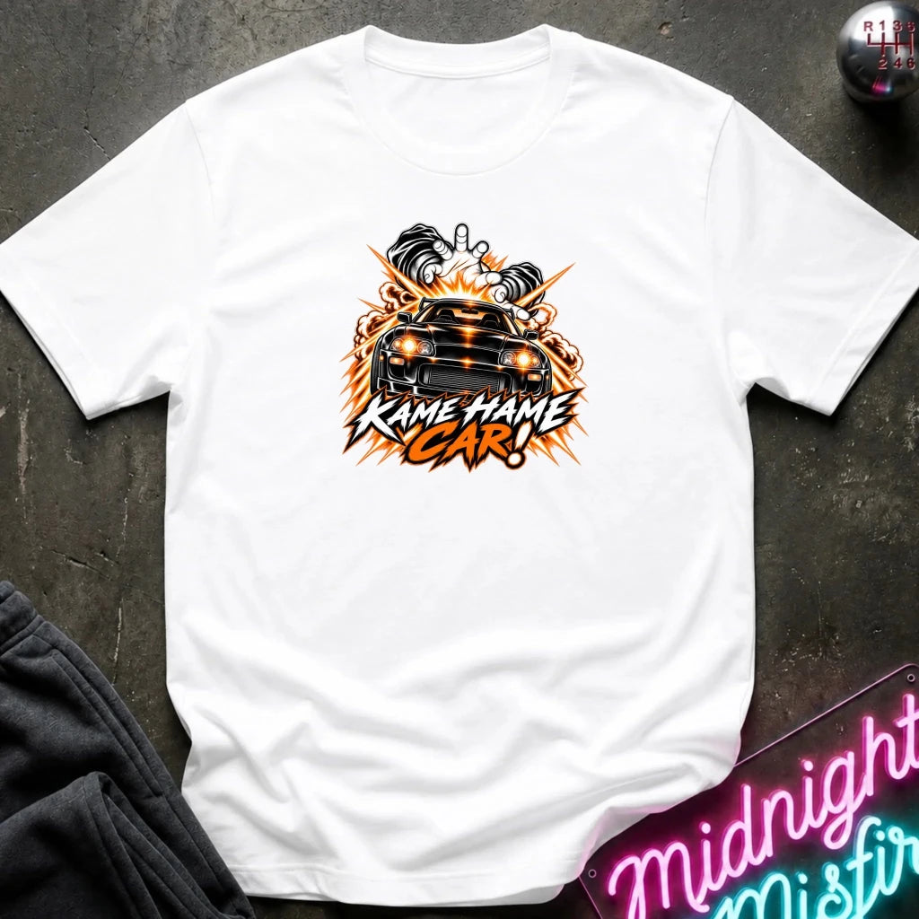 white short-sleeve graphic t-shirt laid flat on a dark textured surface. The shirt features a red, white, and black graphic of a car with the text 'KAME HAME CAR!' in stylized lettering.
