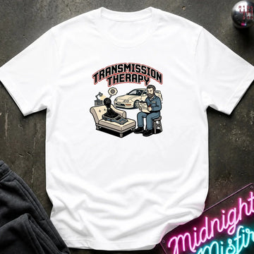 A white short-sleeve graphic t-shirt laid flat on a dark textured surface. The graphic features the text 'TRANSMISSION THERAPY'