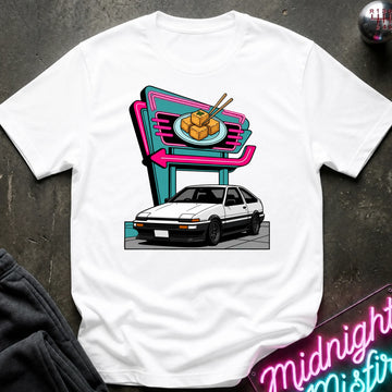 A white short-sleeve crewneck t-shirt featuring a retro-style graphic of a white sports car parked in front of a neon sign. The shirt is displayed flat on a dark textured surface with a dark sweatshirt and a neon sign partially visible as props.