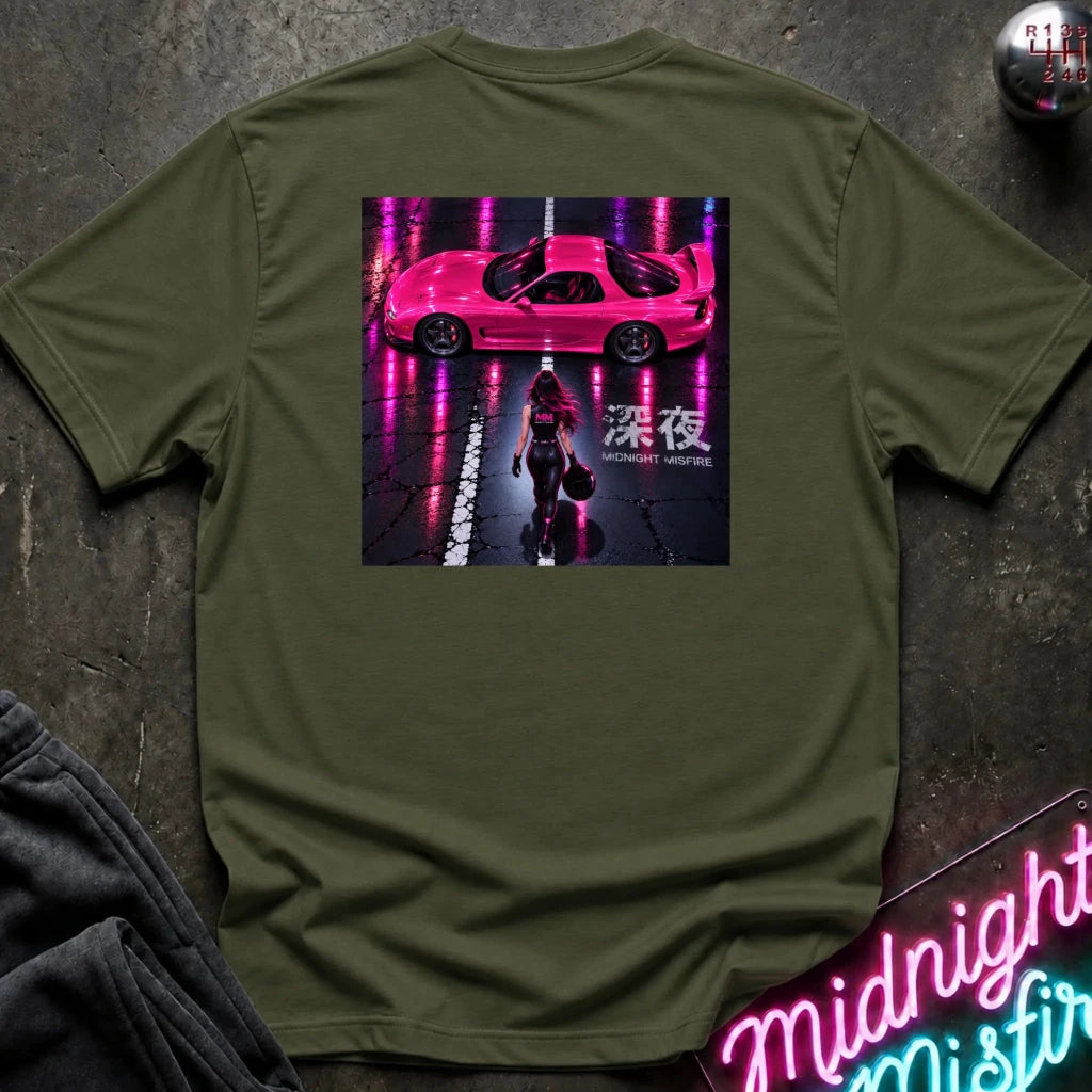 An olive green crewneck t-shirt laid flat on a dark textured surface, featuring a large rectangular graphic print on the back with a pink sports car and a woman walking under neon pink reflections.